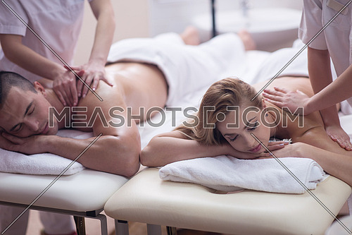Relaxed young beautiful couple receiving a back massage from masseur in a spa