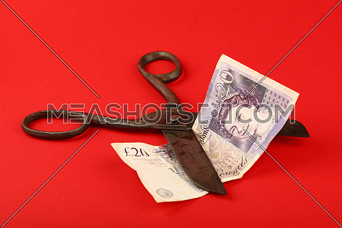 UK and Great Britain financial crisis, decline of British economy and pound illustrated, old vintage scissors cut twenty pounds banknote over red
