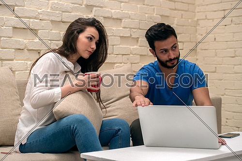 A young man and young lady sitting at home using a laptop