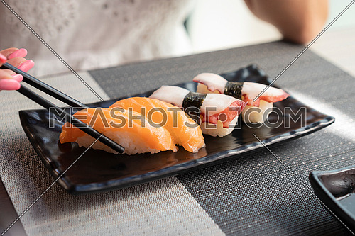 Traditional japanese nigiri sushi with salmon placed between chopsticks and sushi with octopus on black plate