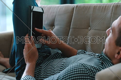 man laying on couch in luxuary villa and using tablet