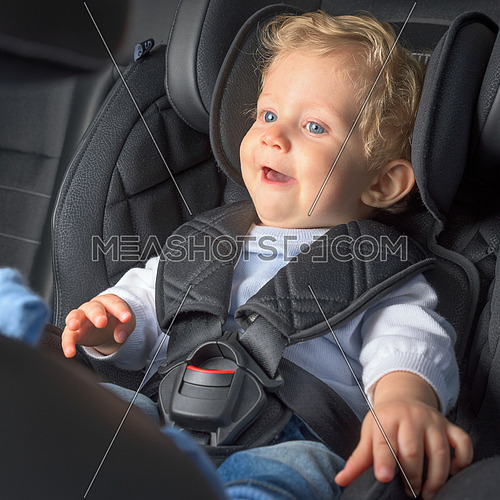 Baby boy 8 months old smiling in a safety car seat.