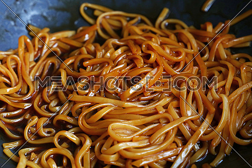 Cooking Asian traditional meal of stir fried udon noodles with soy sauce in wok pan, close up, high angle view