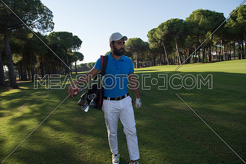 handsome middle eastern golf player carrying and bag  and walking at course on beautiful morning sunrise