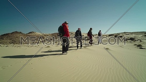 Follow shot for group of tourists walking on sands with bedouin guide while exploring Sinai Trail from Ain Hodouda at day.