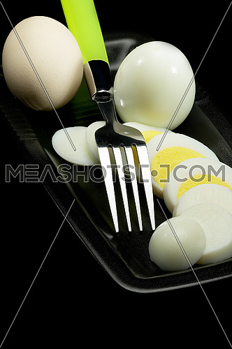 fresh boiled eggs one whole ,one peeled and another sliced on a black plate with fork