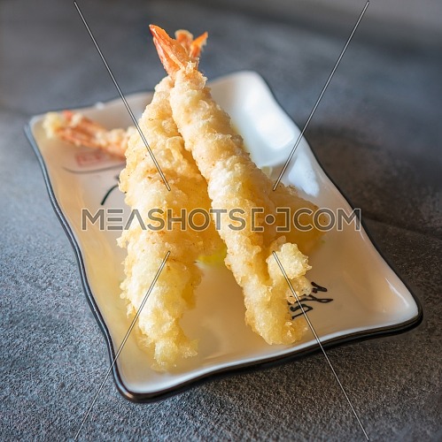 Tempura shrimps served on rectangular white plate on dark gray stone background