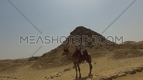 Tracking shot for Saqqara Pyramid showing to camel riders waving  in Giza at day.