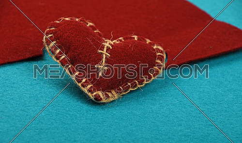 Felt craft and art, one handmade brown stitched toy heart with cut out on blue felt background, low angle view