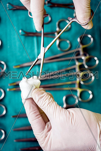Surgeon working in operating room, hands with gloves holding scissors with torunda, conceptual image, vertical composition