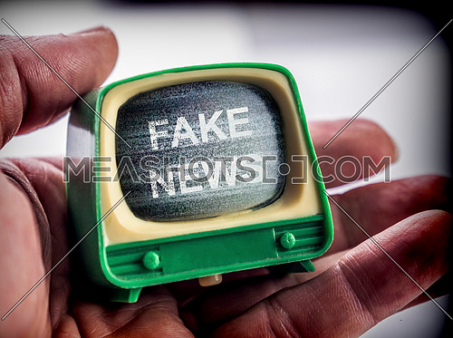 Hand holds miniature TV, fake news metaphor, conceptual image