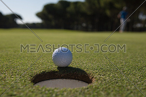 golf ball on edge of course hole representing achivement and success business concept