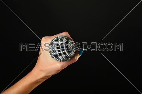 Woman hand with blue nails holding microphone isolated on black background