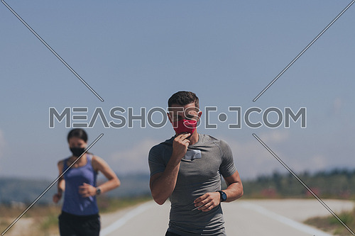 Young man and woman in protective masks running and doing exercises outdoors in the morning. Sport Active life Jogging during quarantine. Covid-19 new normal. Selective focus.