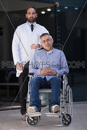 middle eastern sick man in a wheelchair and a young doctor in front of a large modern hospital