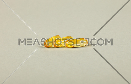 Close up three yellow Omega 3 vitamins and essential fish oils gel cap pills over grey background with copy space, high angle view