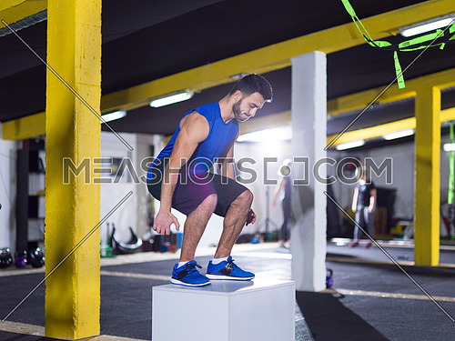 young athletic man training  jumping on fit box at crossfitness gym