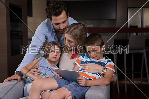happy couple spending time with kids using tablet computer on an armchair  at home