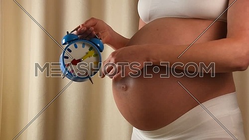 Close up profile view of pregnant Caucasian woman with exposed belly and hands showing clock ticking, slow motion