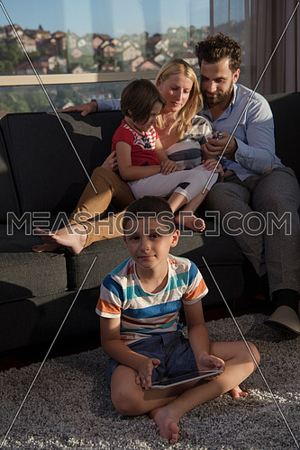 happy couple spending time with kids using tablet computer on sofa at home