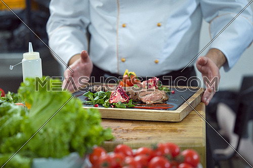 closeup of Chef hands in hotel or restaurant kitchen serving beef steak with vegetable decoration