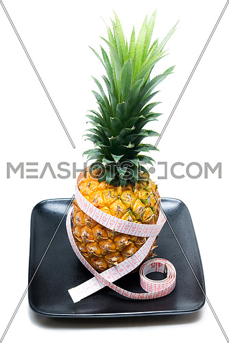 ripe vivid pineapple on a black plate with tape meter