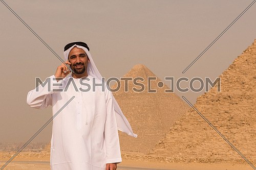 young middle eastern businessman  speeking by phone with egyptian giza pyramids in background
