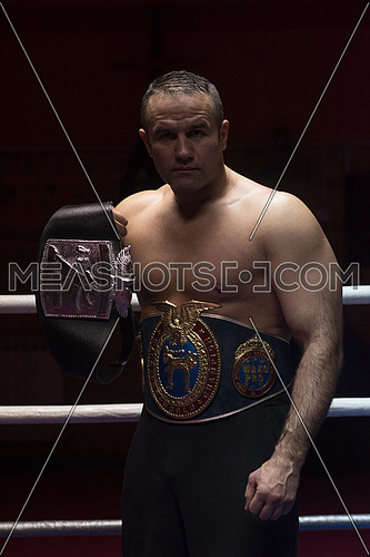 portrait of muscular professional kick boxer with his championship belt in the training ring