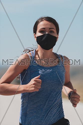Fitness woman in tight sporty clothes wearing black protective face mask running outdoors in the city during coronavirus outbreak. Covid 19 and physical jogging activity, sport and fitness. New normal