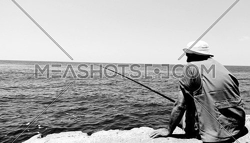 Man siting on the shore fishing in the sea