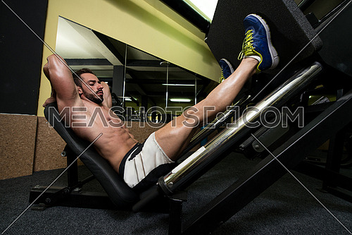 Young Man Using The Leg Press Machine At A Health Club In Gym