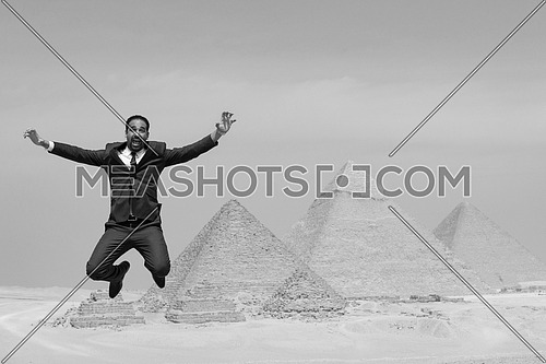 black and white image of arabian business man jumping in desert with pyramids in background