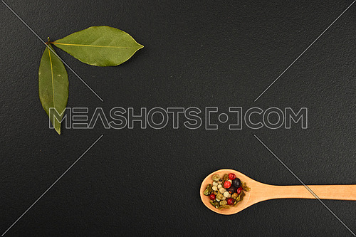 Group of bay two laurel leaves and mix of peppercorn in wooden spoon on black chalkboard background