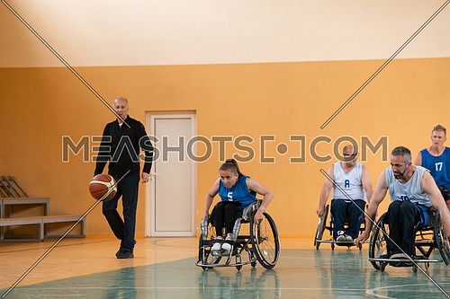 Disabled War veterans mixed race opposing basketball teams in wheelchairs photographed in action while playing an important match in a modern hall. High quality photo.