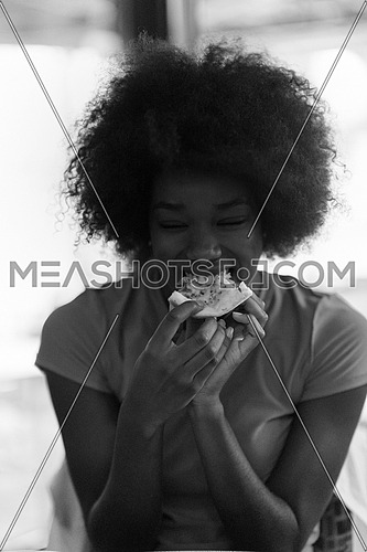 young very hangry african american woman with afro hairstyle eating tasty pizza slice in fast food restaurant