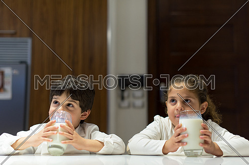 little middle east boy and girl eating snacks and drinking milk in the kitchen with pleasure