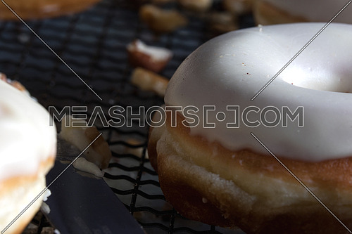 Side view of donuts with white glaze and nuts on a net