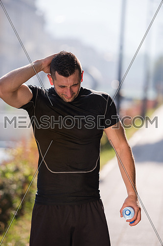 Athlete man runner pouring water from bottle on his head after jogging in the city on a sunny day
