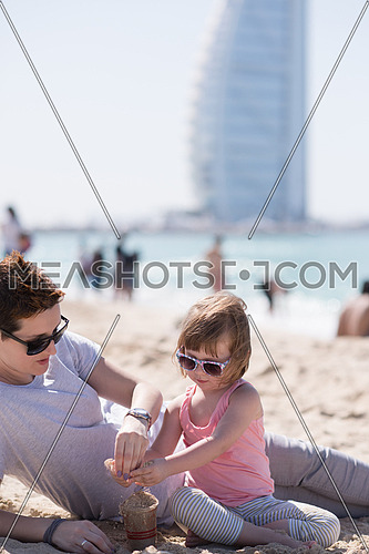 cool young mom and her little girl playing with a bucket full of sand wearing sunglasses and relaxing on the beach on a sunny day
