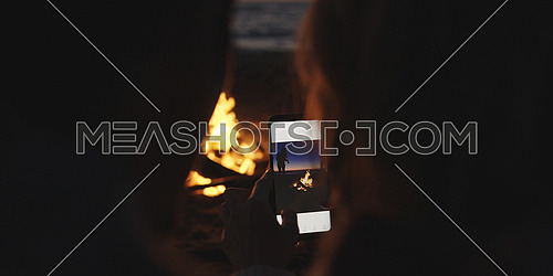 Boy Shows Girl A Picture On His Phone beside campfire on beach