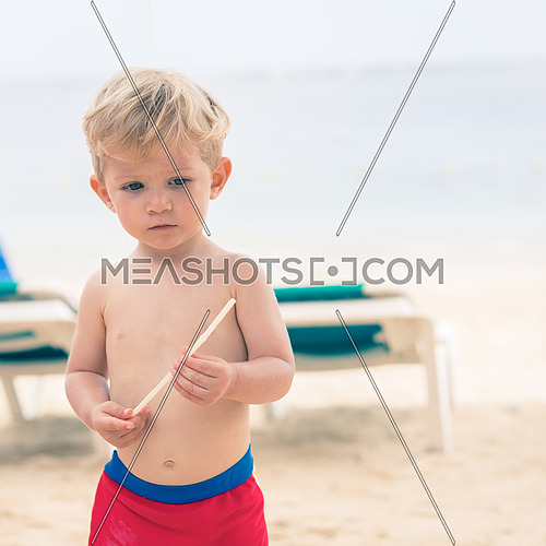 Amazing baby boy on the beach looks at his straw,used split toning for vintage style.