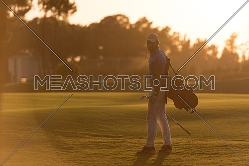 handsome middle eastern golfer  carrying  bag  and walking  to next hole at golf  course on beautiful sunset in background