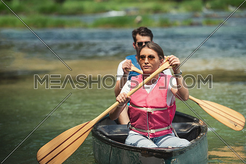 Couple friends are canoeing in a wild river surrounded by the  beautiful nature