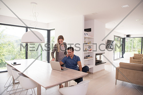 Young couple using laptop computer at luxury home together, looking at screen, smiling.