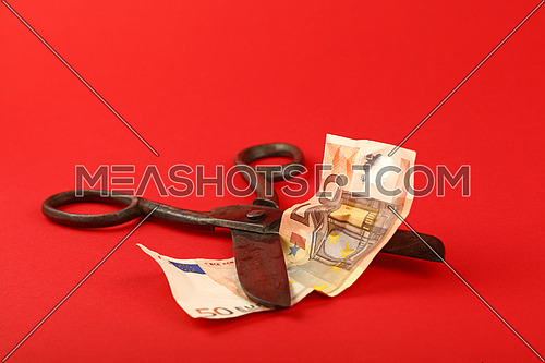 Europe financial crisis, decline of European economy and Euro exchange rate illustrated, old vintage scissors cut fifty EUR banknote on red background