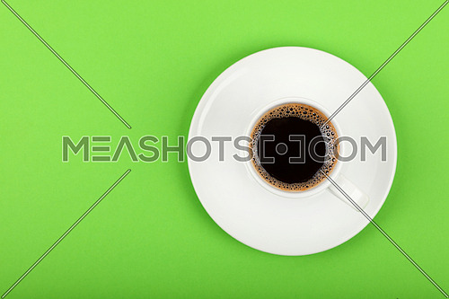 Close up one white cup full of black coffee on saucer over green background, elevated top view, directly above
