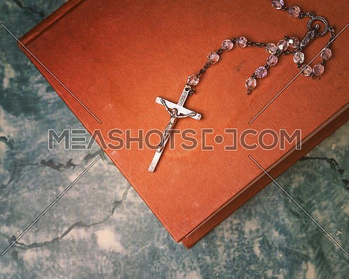 Silver rosary and cross resting on the closed book at green table, seen from above.religion school concept.Vintage style.