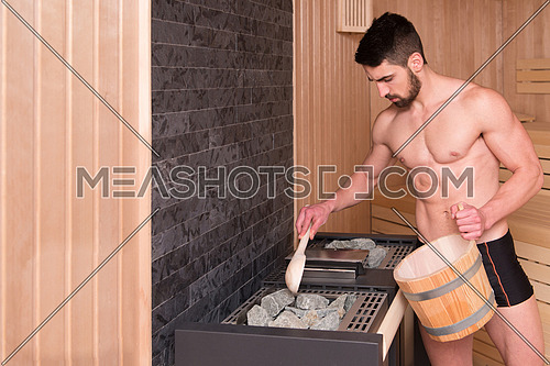Happy Good Looking And Attractive Young Man With Muscular Body Pouring Water On Hot Rocks In Sauna