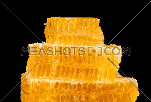 Close up stack of several fresh cut golden comb honey slices on plate isolated on black background, low angle, side view