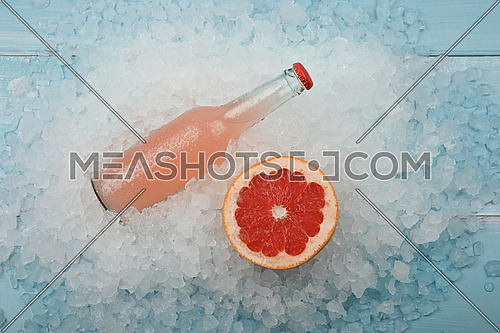Close up one glass bottle of cold pink cocktail with cut slice of orange on crushed ice at retail display, elevated high angle view